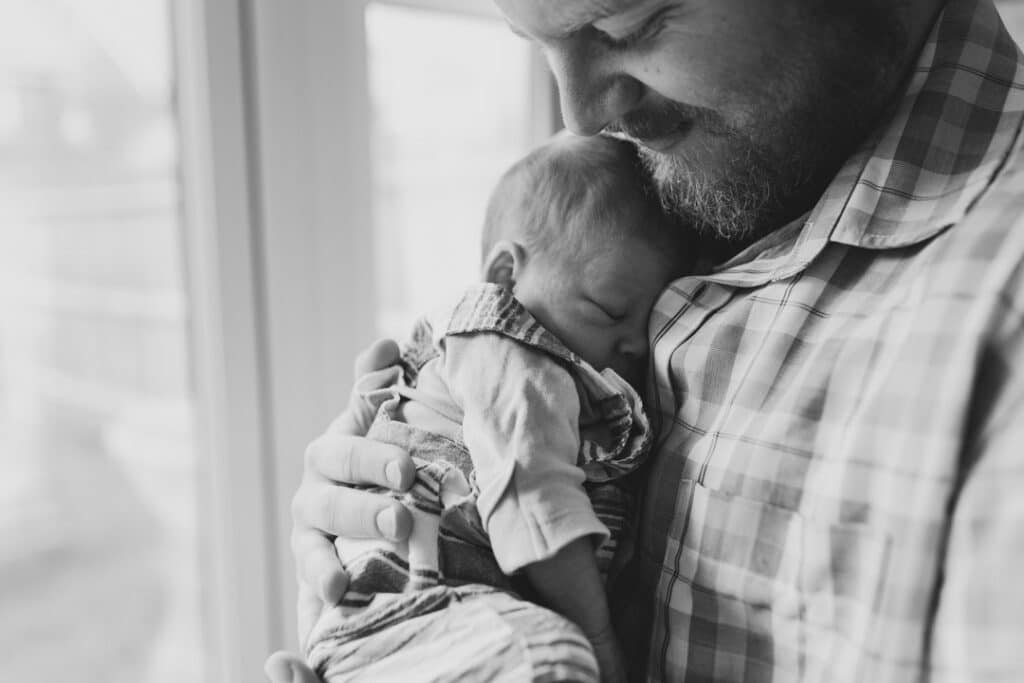 Dad is holding his newborn baby boy close to his chest. Baby boy is sleeping. Newborn photographer in Hampshire. Ewa Jones Photography