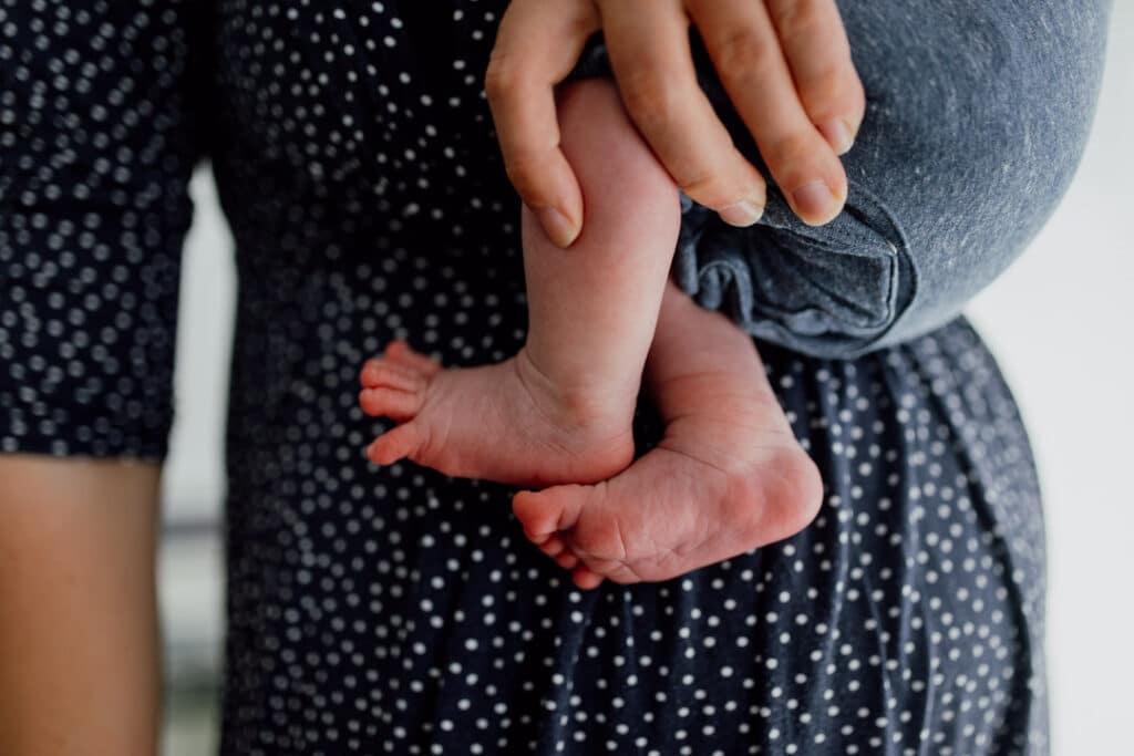 Detail shoot of a newborn baby feet. Baby is held by her mum. Mum is wearing blue dress with white dots. Ewa Jones Photography