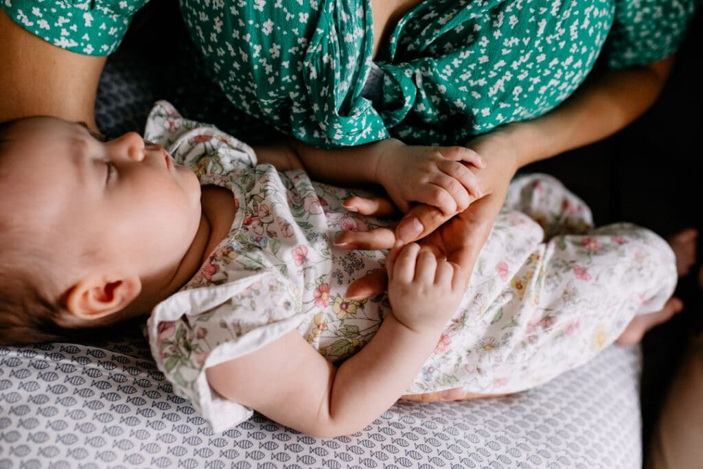 Mum is holding her newborn baby girl fingers. Mum is wearing green dress and baby is wearing lovely flowery baby grow. Newborn photographer in Hampshire. Ewa Jones Photography
