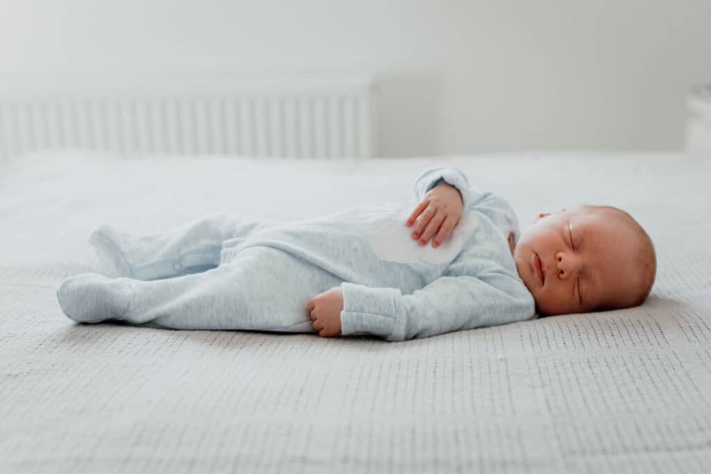 Newborn baby is laying on the bed and sleeping. He is wearing blue baby grow. What to wear for your newborn baby photo shoot. Hook, Hampshire. Ewa Jones Photography