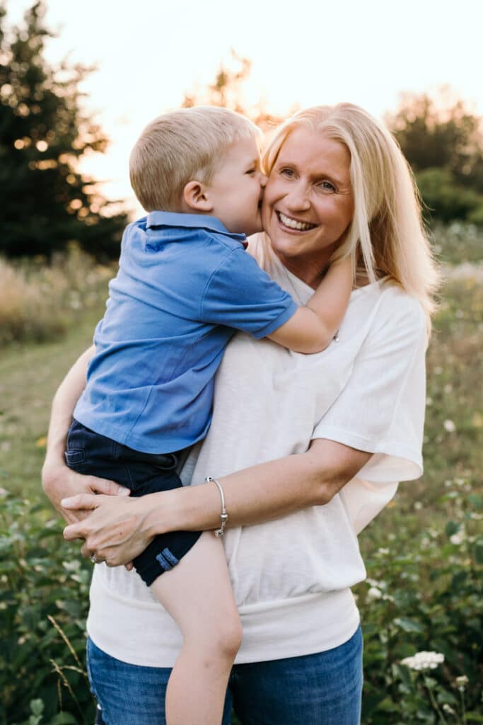 Mum is holding her little boy and boy is kissing mum on her cheek. Mum is wearing white top and jeans and boy is wearing blue top and shorts. Five tips on how to prepare for a family photo session. Family photographer in Hampshire. Ewa Jones Photography