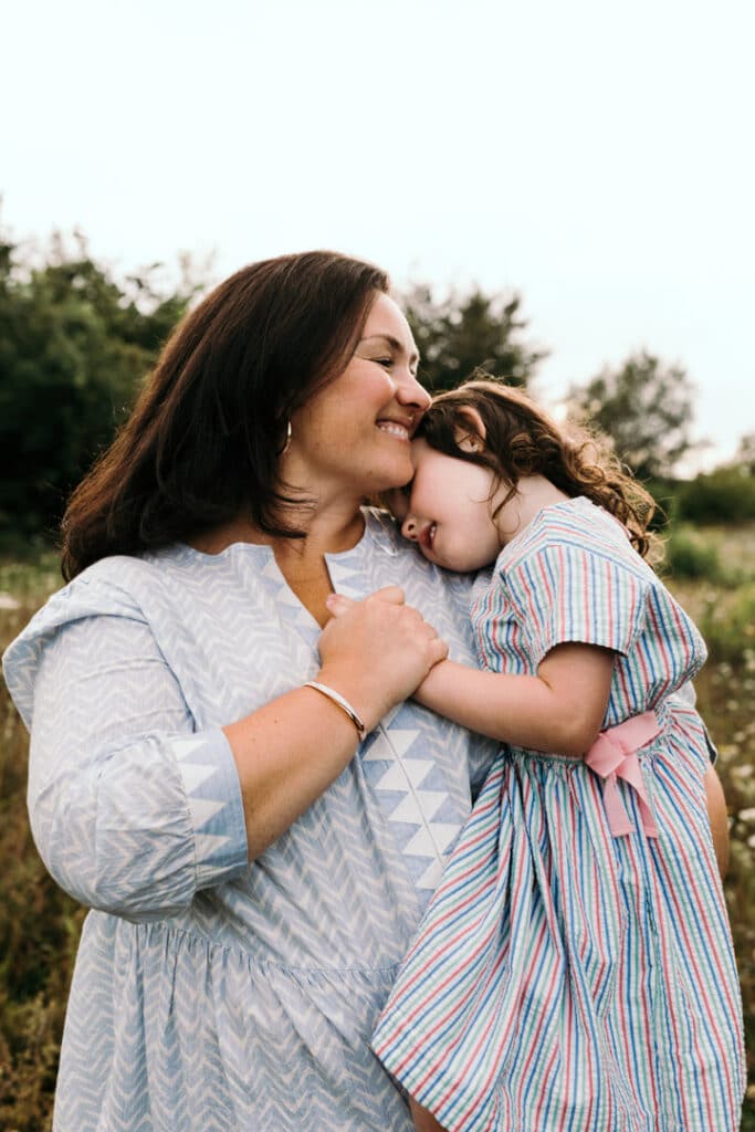 Mum is holding her daughter and is holding her hand close to her chest. Mum is smiling and daughter head is resting on mums shoulders. Lovely mum and daughter moment. Family photography in Basingstoke, Hampshire. Ewa Jones Photography