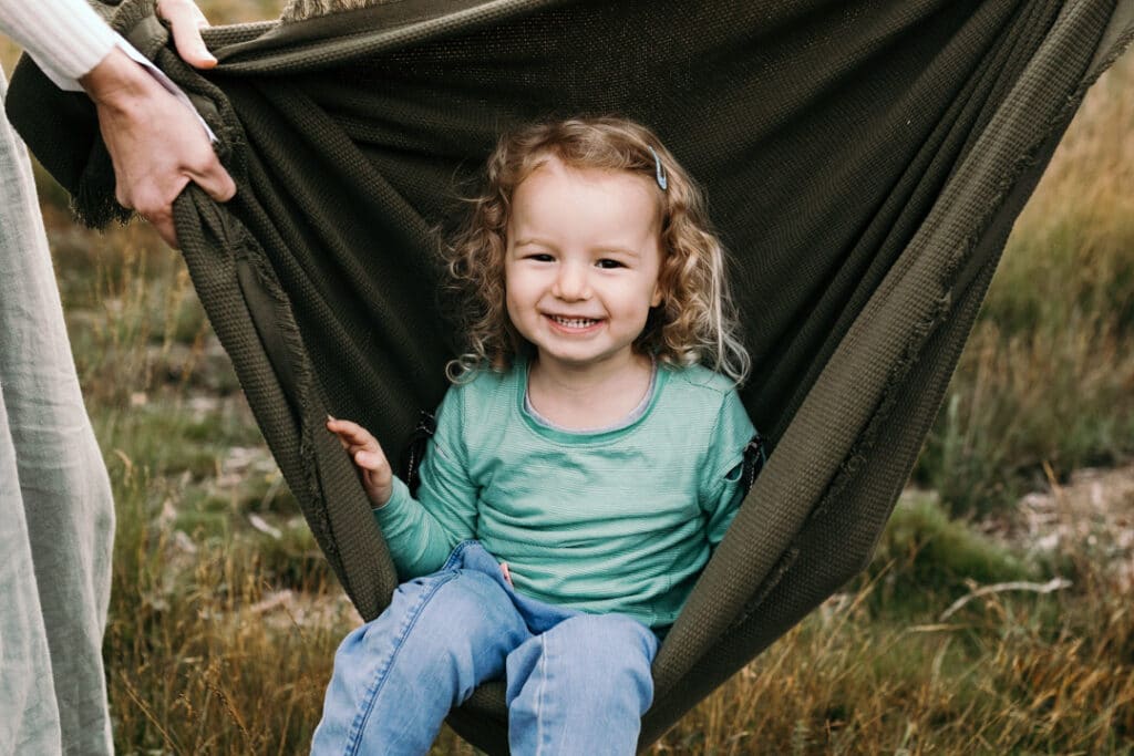 Little girl is sitting inside the blanket and smiling at the camera. Family photographer in Hampshire. Ewa Jones Photography