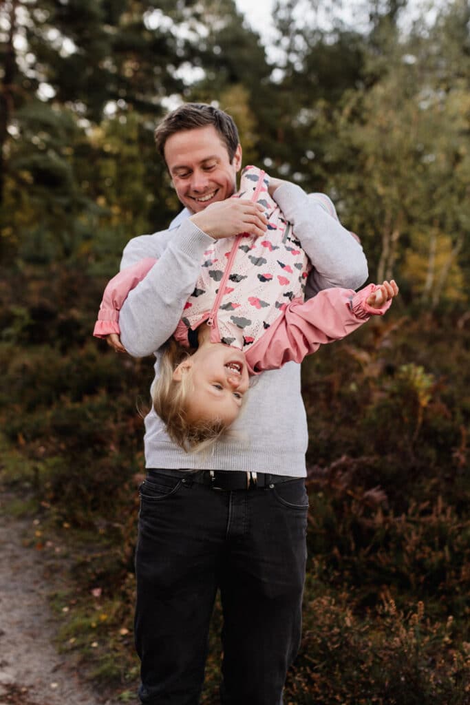 Dad is holding her little girl upside down. Little girl is laughing. Autumnal photo session in Surrey. Five tips on how to prepare for a family photo session. Ewa Jones Photography