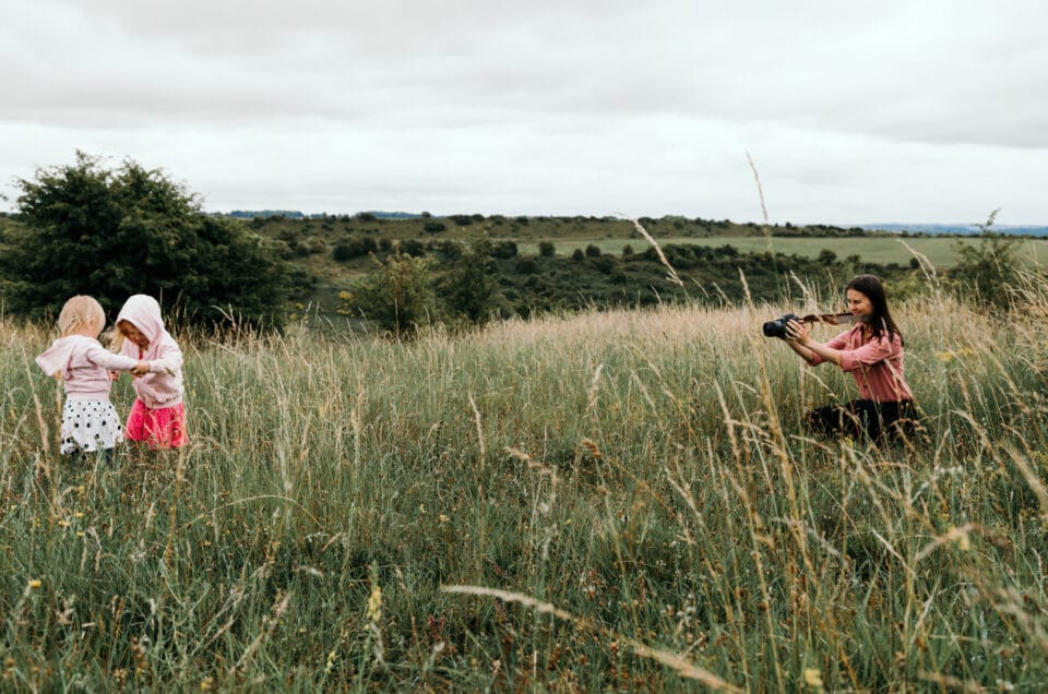 Photographer is holding camera out and taking video of two little girls. It's warm day and long grass on the ground. Review of my 2020 photography goals. Ewa Jones Photography