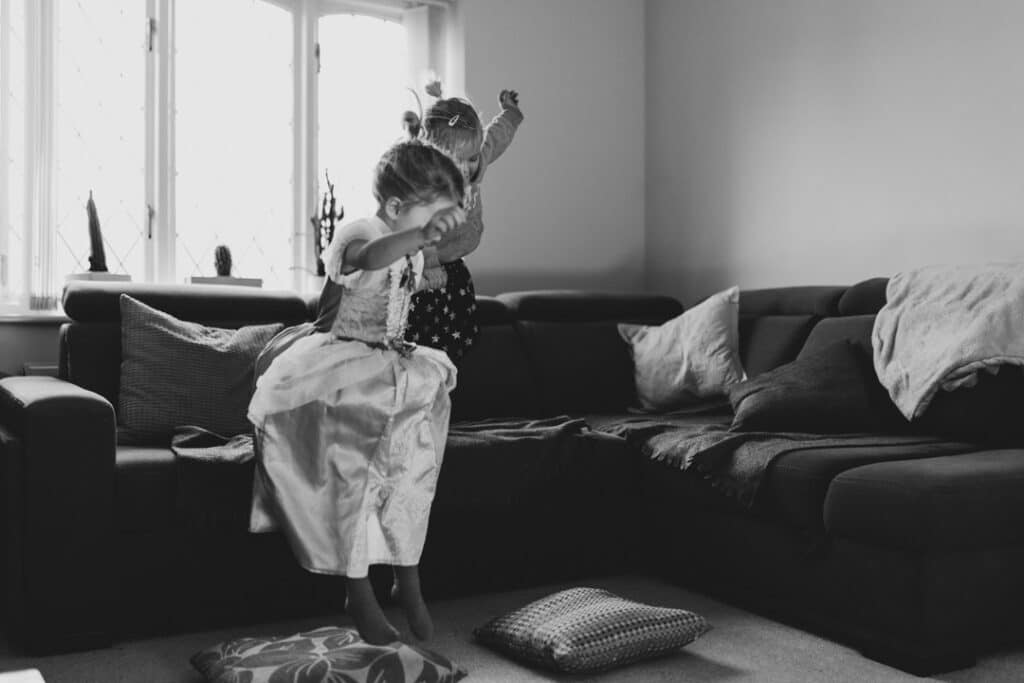 Two girls are jumping off the sofa. Black and white photography. Family photographer in Basingstoke, Hampshire Ewa Jones Photography.