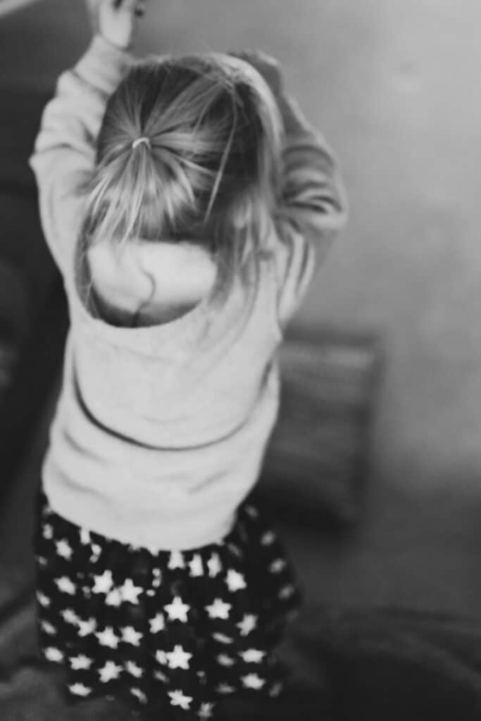 Little girl is getting ready to jump off the sofa. Natural family photography in Hampshire. Ewa Jones Photography