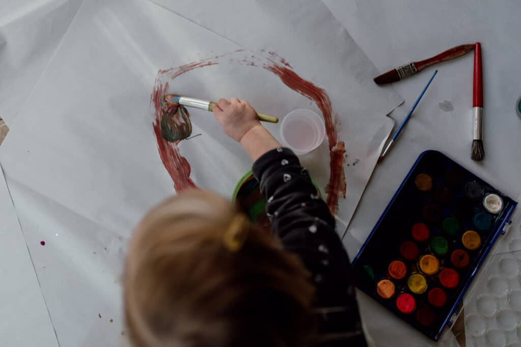 Little girl is painting big pieces of paper. she is making a circle. Family photographer in Hampshire. Ewa Jones Photography
