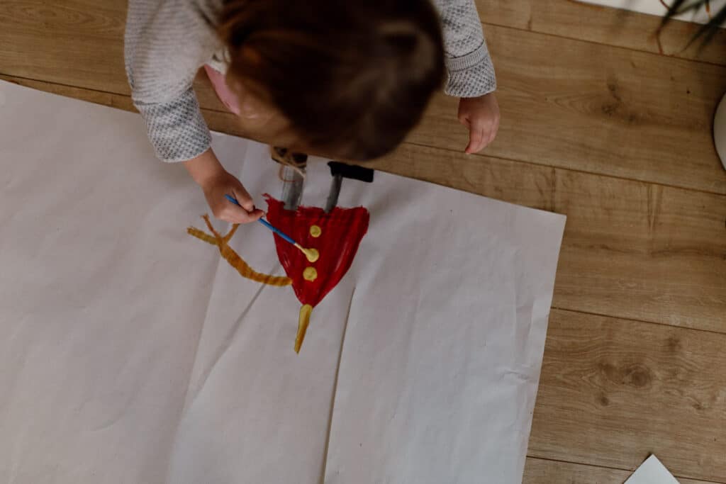 Looking up at the picture the little girl is drawing. She is drawing a little girl in a red dress. Family photographer in Basingstoke, Hampshire. Ewa Jones Photography