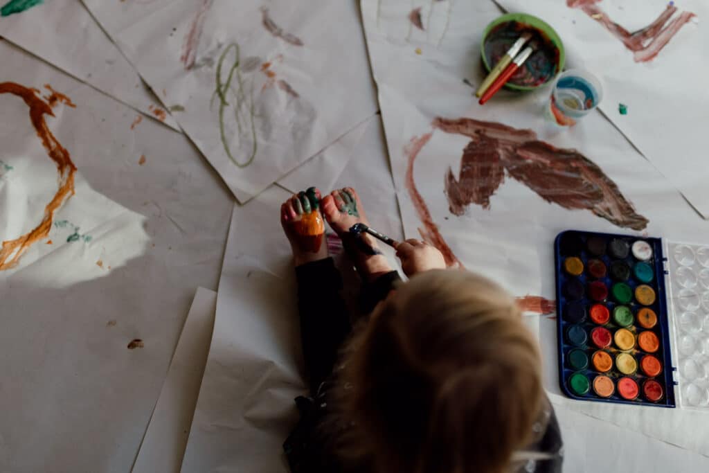 Little girl is painting her feet and sun is shining on her feet. 7 tips on photographing kids at home. Family photography in Hampshire. Ewa Jones Photography