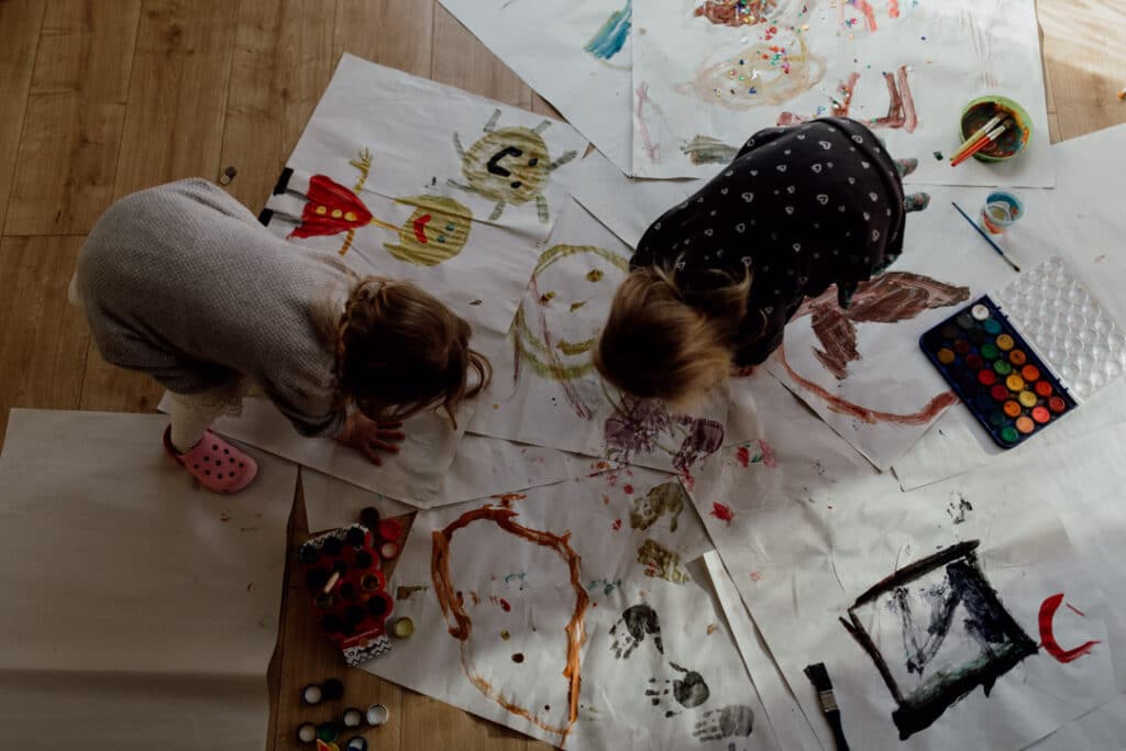 Two girls are painting big pieces of paper. They are doing hand prints. family photographer in Basingstoke, Hampshire. Ewa Jones Photography