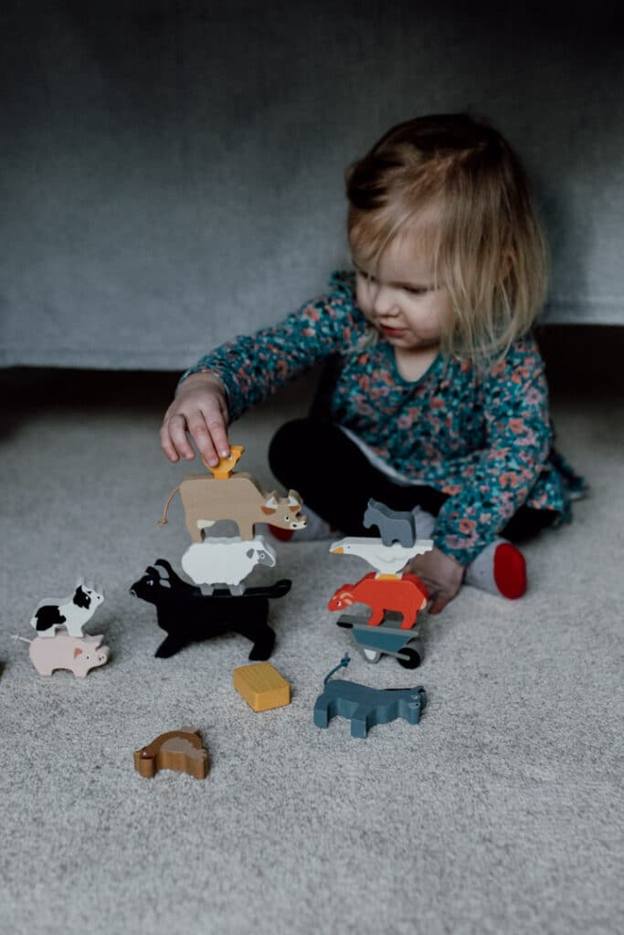 Little girl is playing with farm animals. She is stacking them one animal on to of the other to balance. Lifestyle family photography in Basingstoke, Hampshire. Two sisters are laying on the floor and looking at each other. They are both smiling to each other. 7 tips on photographing kids at home. Family photography in Hampshire. Ewa Jones Photography
