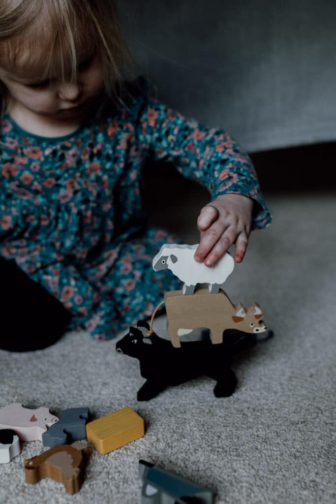 Little girl is playing with farm animals. She is stacking them one animal on to of the other to balance. Lifestyle family photography in Basingstoke, Hampshire. Two sisters are laying on the floor and looking at each other. They are both smiling to each other. 7 tips on photographing kids at home. Family photography in Hampshire. Ewa Jones Photography