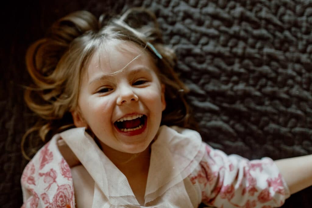 Girl is laughing and laying on the bed. Close up of little girl face. family photographer in Basingstoke. Ewa Jones Photography