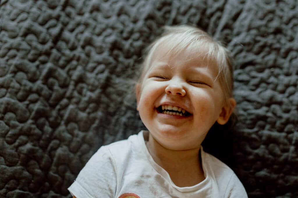 Girl is laughing and laying on the bed. Close up of little girl face. family photographer in Basingstoke. Ewa Jones Photography