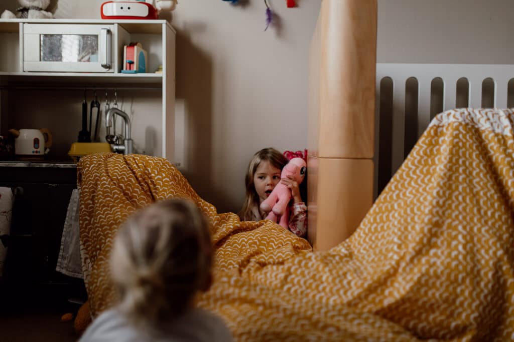 Playing the puppet show with dolls and made up curtain from the duvet. un-posed in home family photography in Hampshire. Ewa Jones Photography