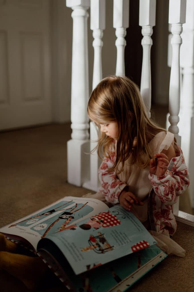 Girl is sitting on the floor and reading a book. Family photography in Hampshire. Ewa Jones Photography