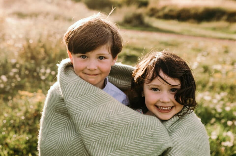 Brother and sister are wrapped around the blanket and looking at the camera. Lovely summer evening. Family photographer in Hampshire. Ewa Jones Photography