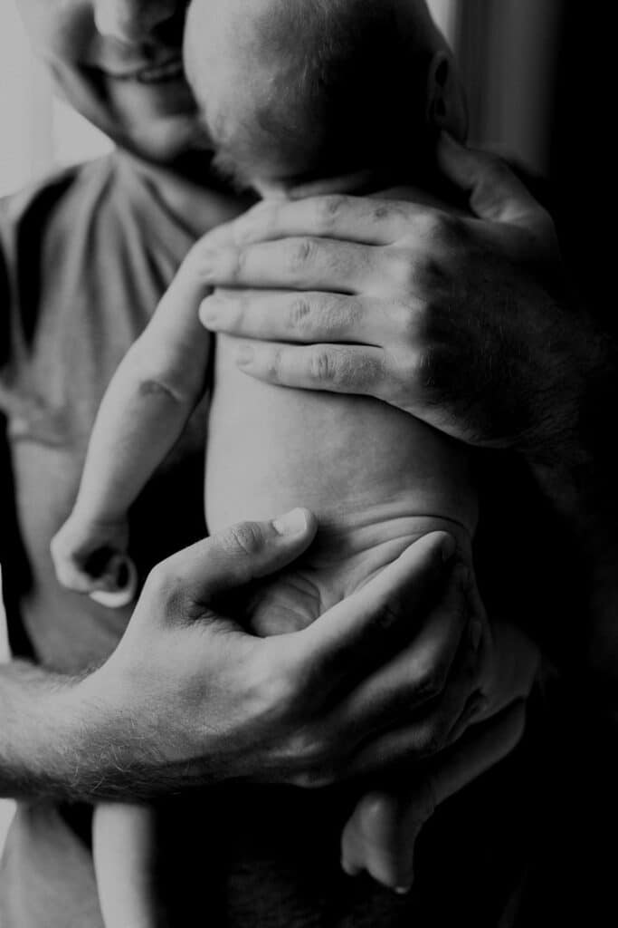 Dad is holding a newborn baby close to his chest. Black and white photography. Newborn baby photo session in Hampshire. Ewa Jones Photography