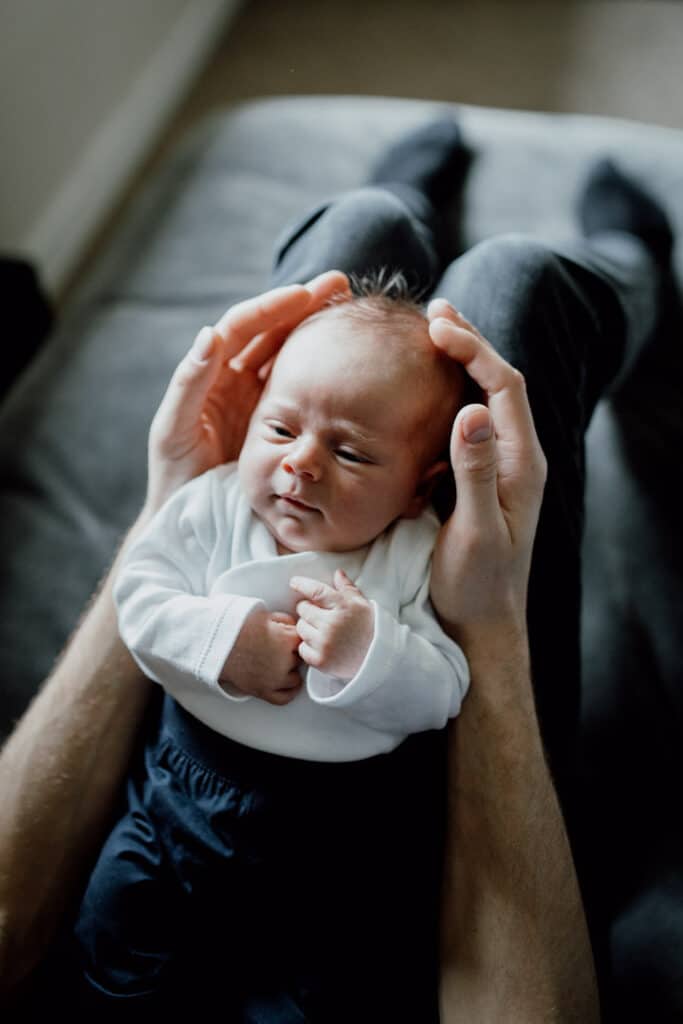 newborn baby is laying on dad's hands. he is looking at his dad lovingly. Newborn baby photo shoot in Basingstoke, Hampshire. Ewa Jones Photography