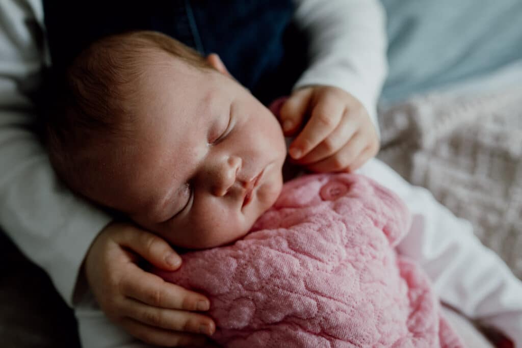 older sister is holding little newborn girl. Newborn baby girl is sleeping. Newborn photographer in Basingstoke, Hampshire. Ewa Jones Photography