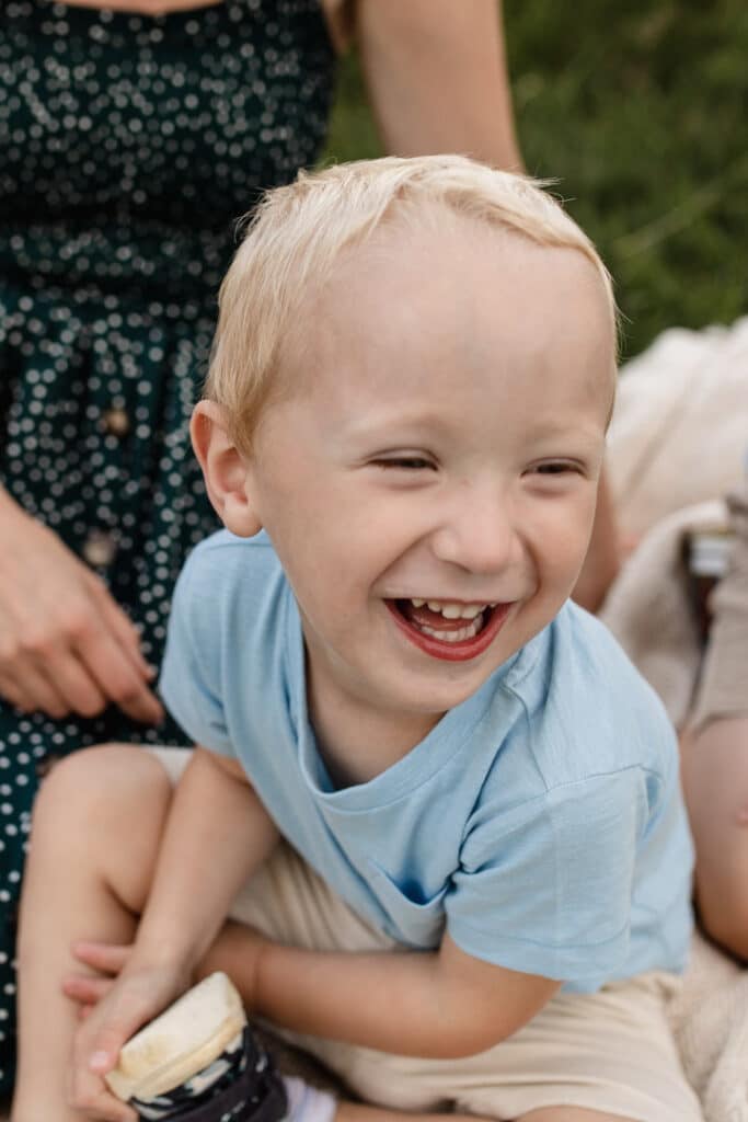 Little boy is sitting on the blanket and laughing. Capturing natural smiles during a family photo session. Family photographer in Hampshire. Ewa Jones Photography