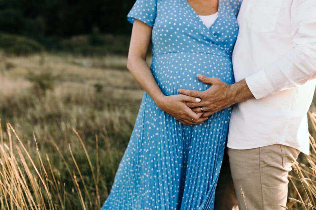 Mum and dad are holding their bump. Expecting mum is wearing lovely blue dress with white spots. Maternity photographer in Hampshire. Ewa Jones Photography