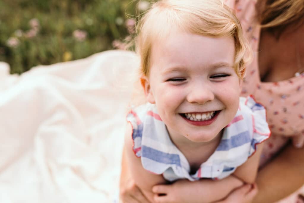Little girl is smiling to the camera. it is lovely summer evening. golden hour family photo session in Hampshire. Ewa Jones Photography
