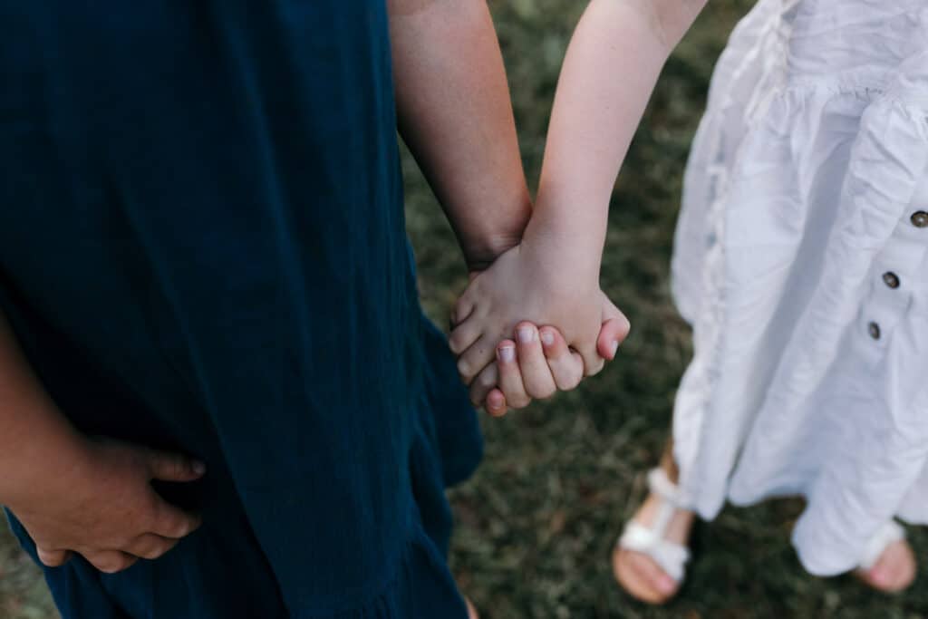 two sisters are holding hands. it is summer evening and they are wearing lovely summer dresses. Golden hour family photo session in Bracknell, Hampshire. Ewa Jones Photography
