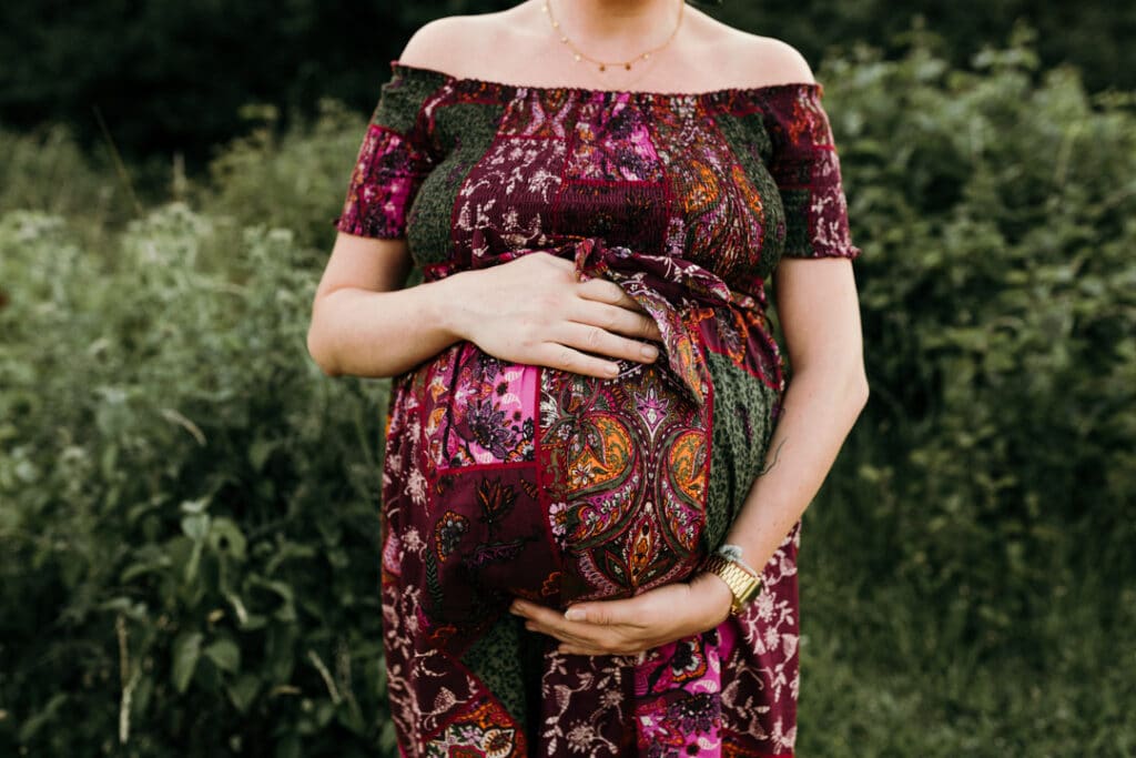 Expecting mum is holding her baby bump. she is wearing a flower dress. Maternity photographer in Basingstoke, Hampshire. Ewa Jones Photography