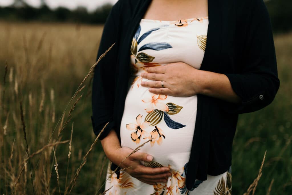 Expecting mum is holding her baby bump. she is wearing a flower dress. Maternity photographer in Basingstoke, Hampshire. Ewa Jones Photography