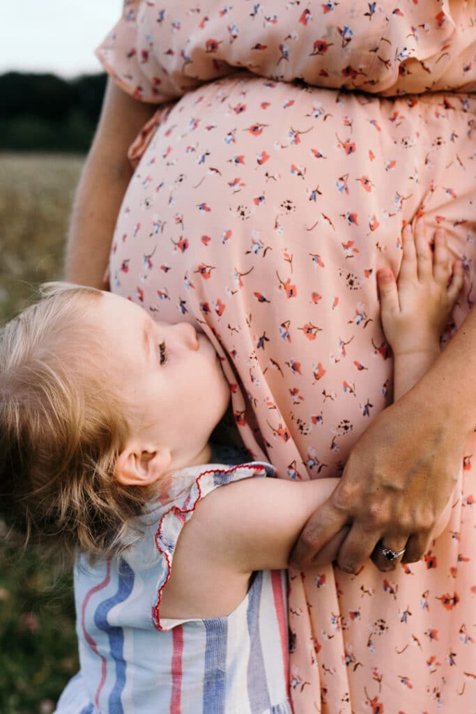 Little girl is kissing baby bump. Expecting mum is wearing lovely maternity dress. Maternity photographer in Hampshire. Ewa Jones Photography