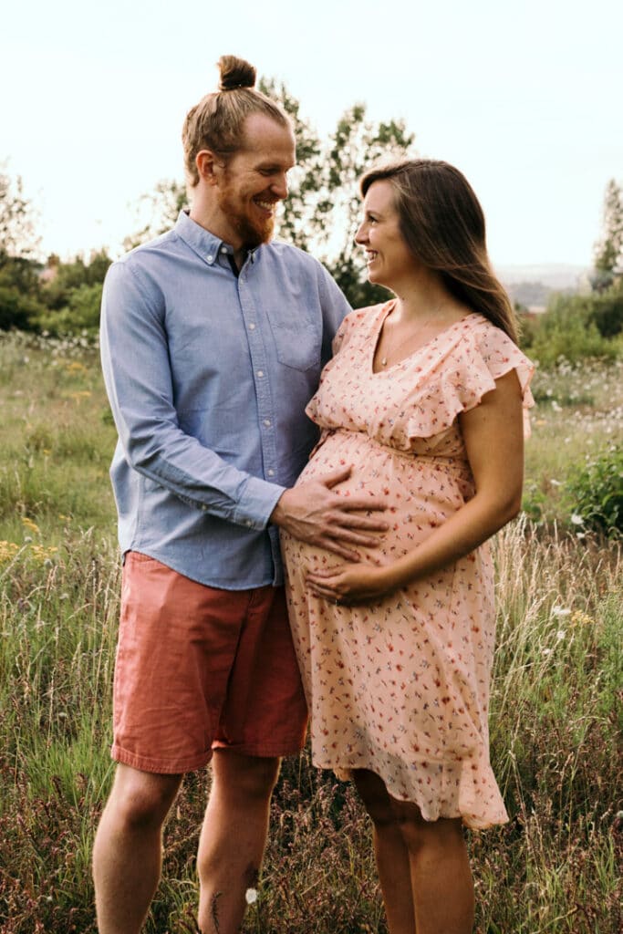 Mum and dad are standing next to each other and looking at each other and smiling. Lovely maternity photo session during golden hour. Maternity photographer in Hampshire. Ewa Jones Photography