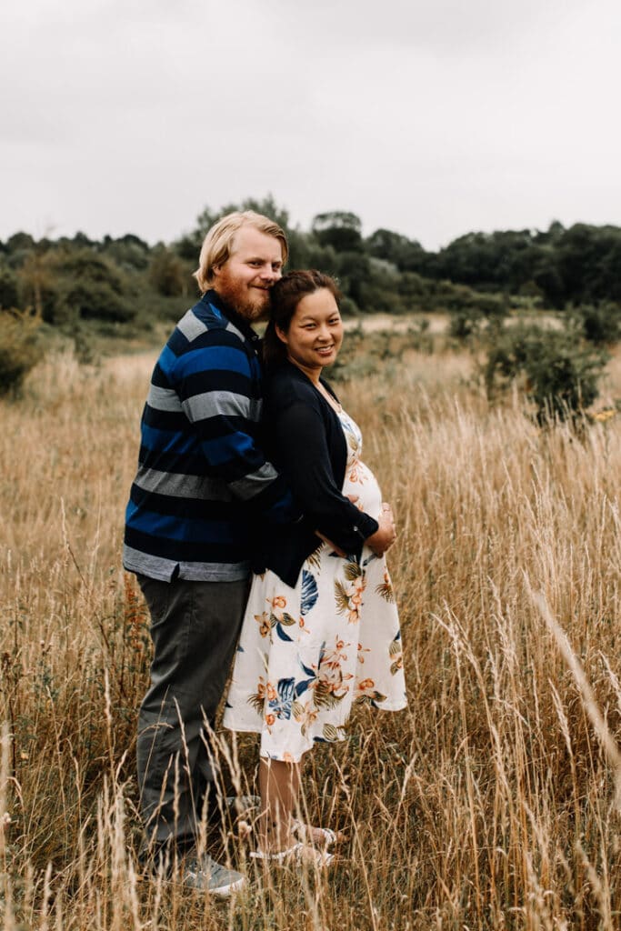 Expecting mum is standing in front of her husband. Maternity photo session in Hook, Hampshire. Ewa Jones Photography