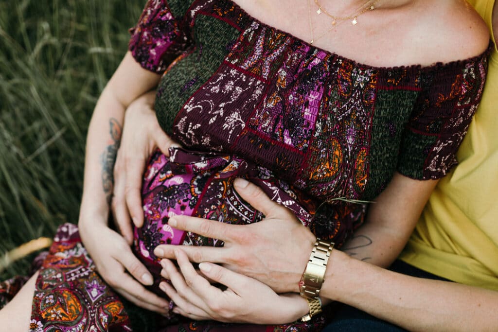 Pregnant mum is sitting down and her husband is sitting behind her. They are both holding baby bump. Maternity photographer in Hampshire. Ewa Jones Photography