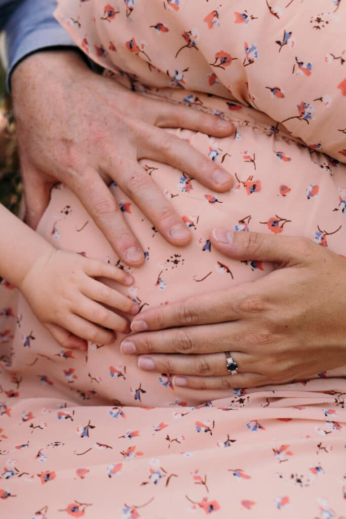 Mum, dad and their toddle girl are all holding baby bump. Expecting mum is wearing lovely salmon colour dress. 7 must-have maternity poses during my maternity photo sessions. Maternity photography in Basingstoke, Hampshire. Ewa Jones Photography