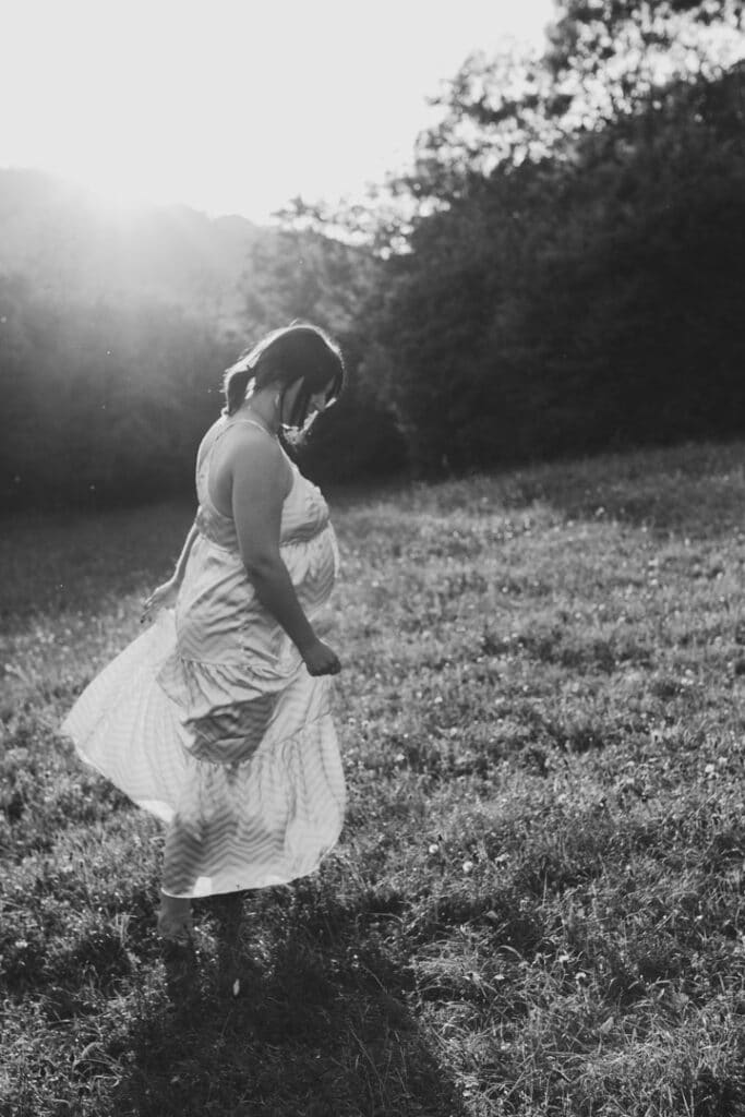 Pregnant mum is standing in the field. she is looking down and holding her dress. Candid maternity photo session. Maternity photographer in Hampshire. Ewa Jones Photography. My top 7 maternity poses