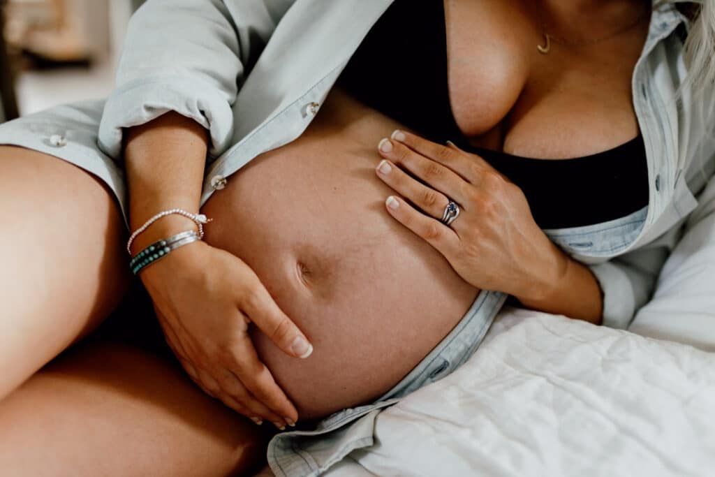 Mum is laying on bed and holding her baby bump. She is wearing a jean top and black bra. Intimate maternity photography in Hampshire. Ewa Jones Photography