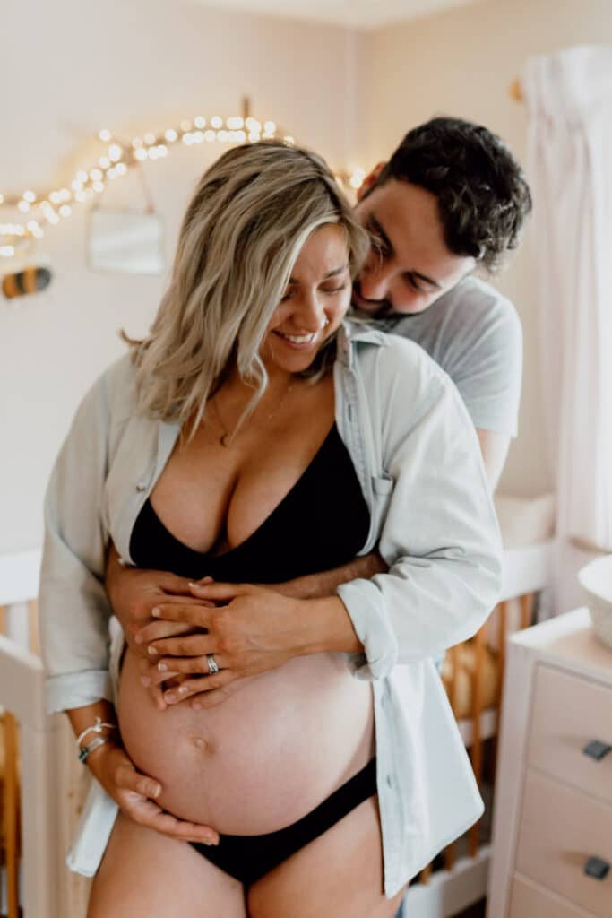 Pregnant mum is standing in baby nursery and her husband is hugging her and baby bump. Lovely in home maternity photography in hampshire. Ewa Jones Photography