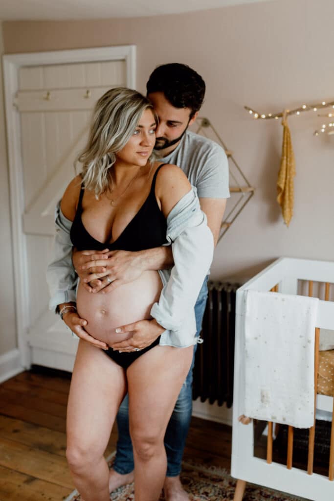 Pregnant mum is standing in baby nursery and her husband is hugging her and baby bump. Lovely in home maternity photography in hampshire. Ewa Jones Photography