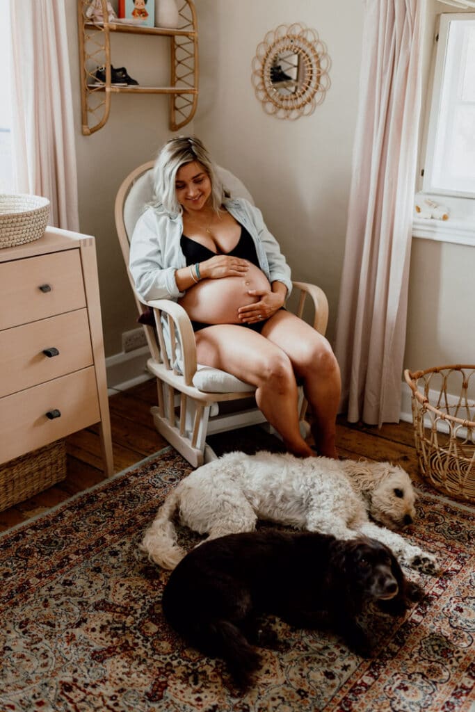 Pregnant mum is sitting on the nursing chair and looking at her two dogs. Lovely maternity photo session in Hampshire. Ewa Jones Photography