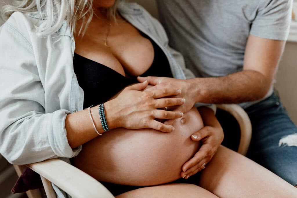 Close up shot of baby bump. Mum is holding a bump and she is wearing a jean jacket and black bra. Intimate maternity photography. Ewa Jones Photography