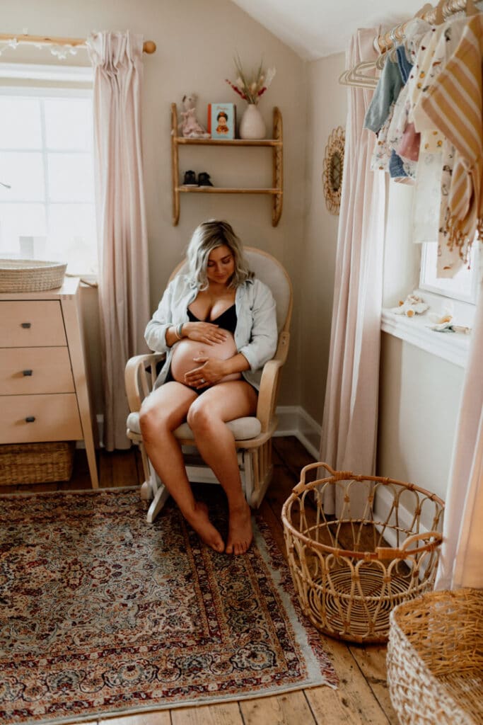 Pregnant mum is sitting in the baby nursery and looking at her baby bump. in home maternity photography in Hampshire. Ewa Jones Photography