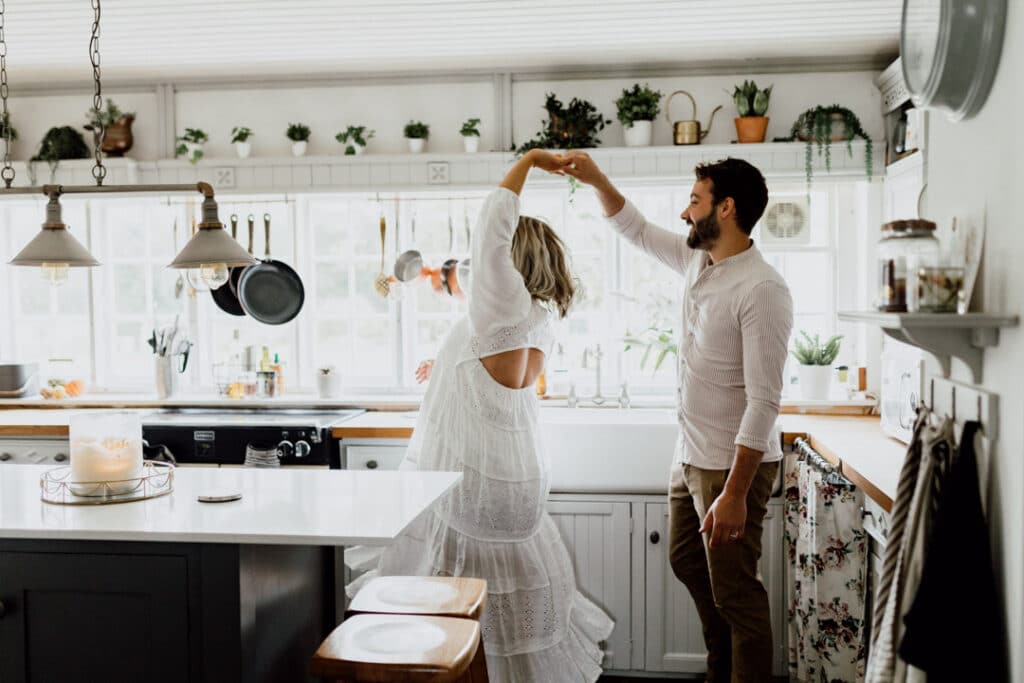 Expecting parents are dancing in the kitchen. Mum is wearing a lovely maternity dress. in home maternity photo session in Hampshire. Ewa Jones Photogrraphy