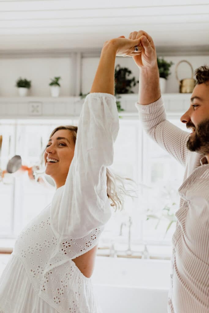 Expecting parents are dancing in the kitchen. Mum is wearing a lovely maternity dress. in home maternity photo session in Hampshire. Ewa Jones Photogrraphy