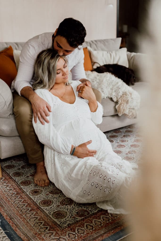 Maternity photography - Laura & Sam. Sam is sitting on the sofa and kissing his wife. She is sitting on the floor and holding her bump. mum to be lovely maternity photography in Hampshire. Ewa Jones Photography