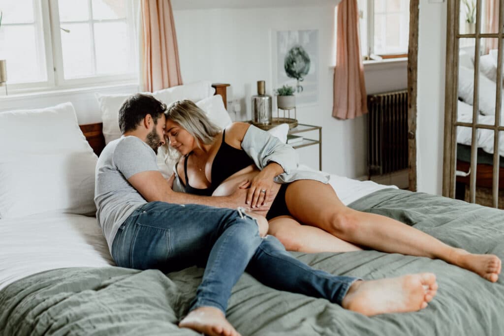 Expecting mum is laying on bed and her husband is holding bump. Lovely in home maternity photography. Ewa Jones Photography