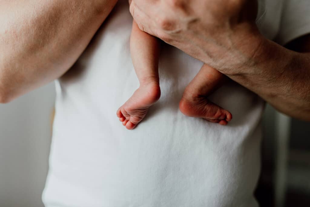 Close up feet detail of a newborn baby feet. Dad is holding the newborn baby and he is wearing a white t-shirt. Newborn baby photography in Hampshire. Ewa Jones Photography