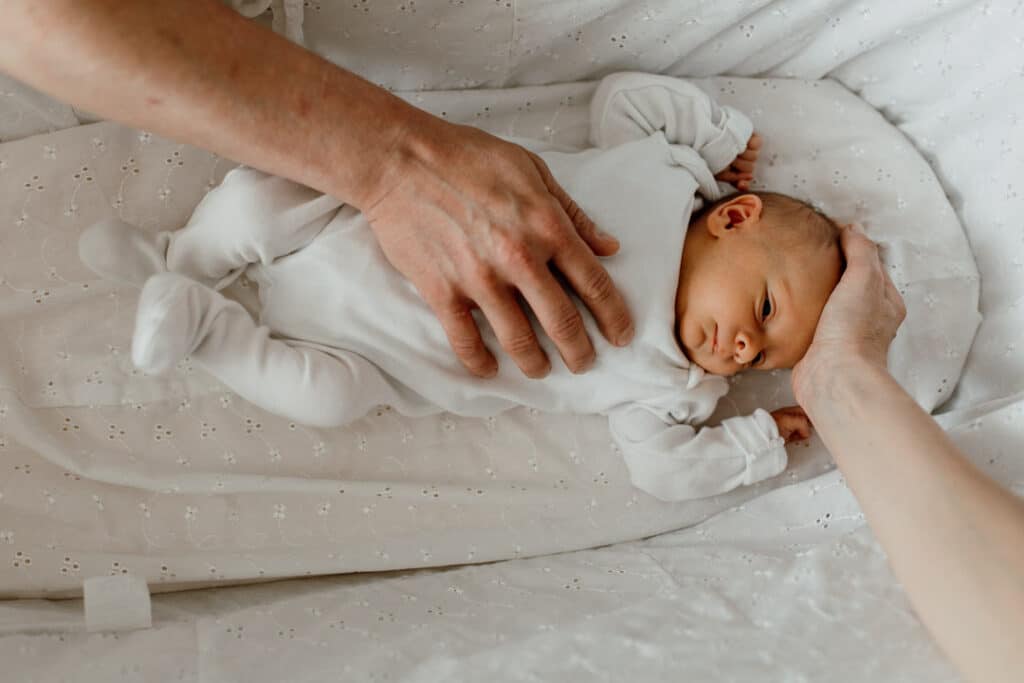 Newborn baby girl is laying in the moses basket and mum and dad are both have their hands placed on the newborn baby. Newborn photographer in Basingstoke. Ewa Jones Photography