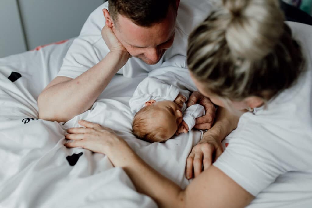 Mum and dad are laying on bed and looking at their newborn baby. Baby is sleeping. Newborn photography in Hampshire. Ewa Jones Photography